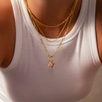 Person in a white tank top wearing layered gold necklaces, one featuring the Ombre Lace Alexandrite Charm and small pendants including an angel.