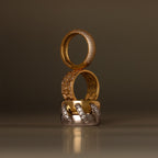 The Sculpted Mixed Metal Link Ring, adorned with pavé diamonds, is stacked with two other gold and diamond rings against a blurred brown background.