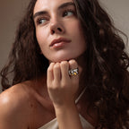 A woman with long curly hair rests her chin on her hand, wearing the Sculpted Mixed Metal Link Ring and gazing to the side.