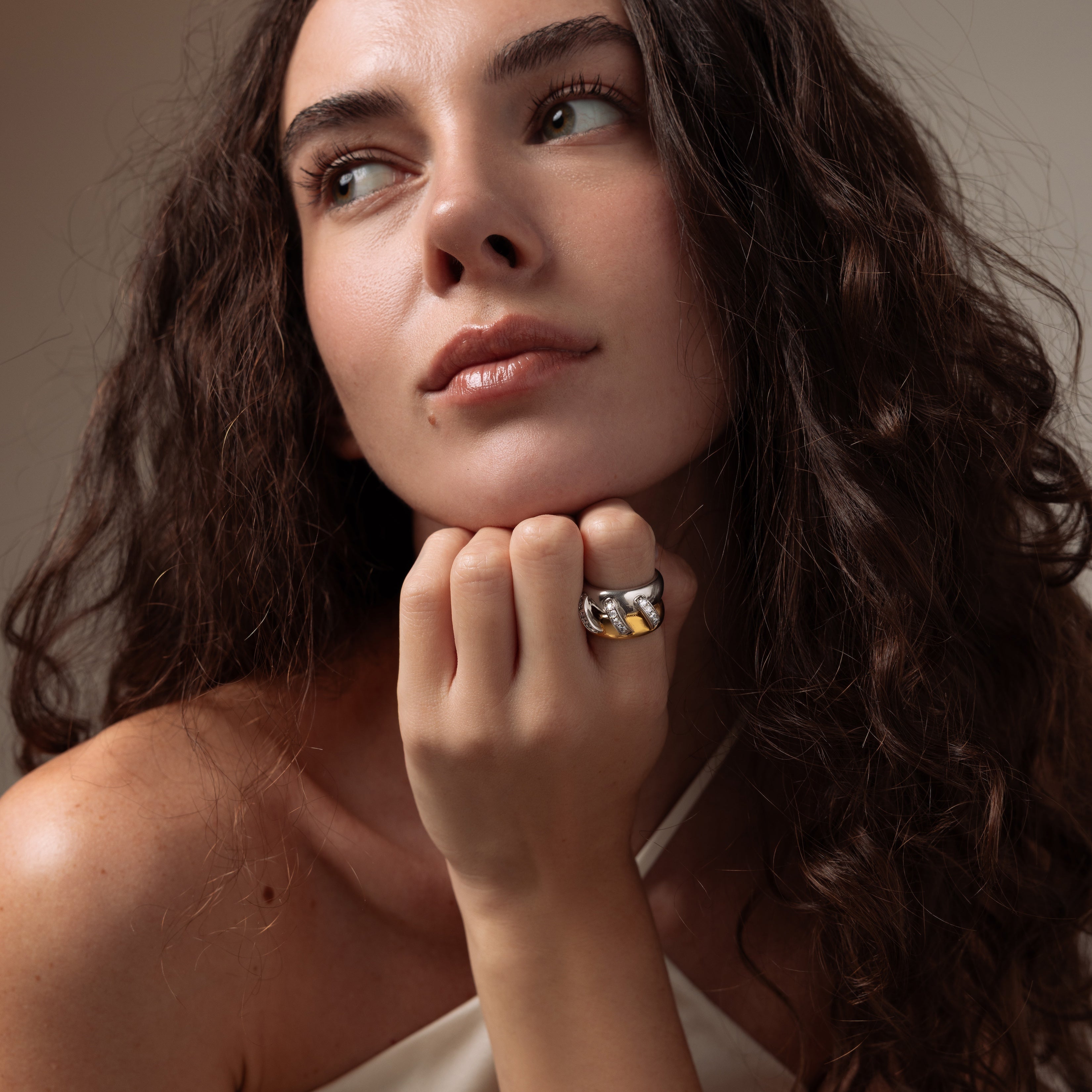 A woman with long curly hair rests her chin on her hand, wearing the Sculpted Mixed Metal Link Ring and gazing to the side.