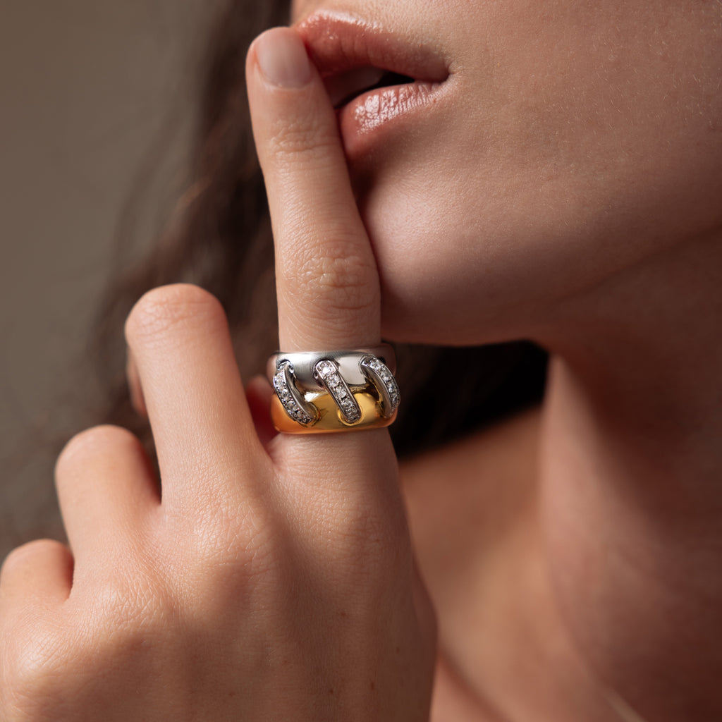 Woman touching her lips, wearing the Sculpted Mixed Metal Link Ring—a chunky piece featuring mixed metals, embedded gemstones, and pavé diamonds—on her finger.