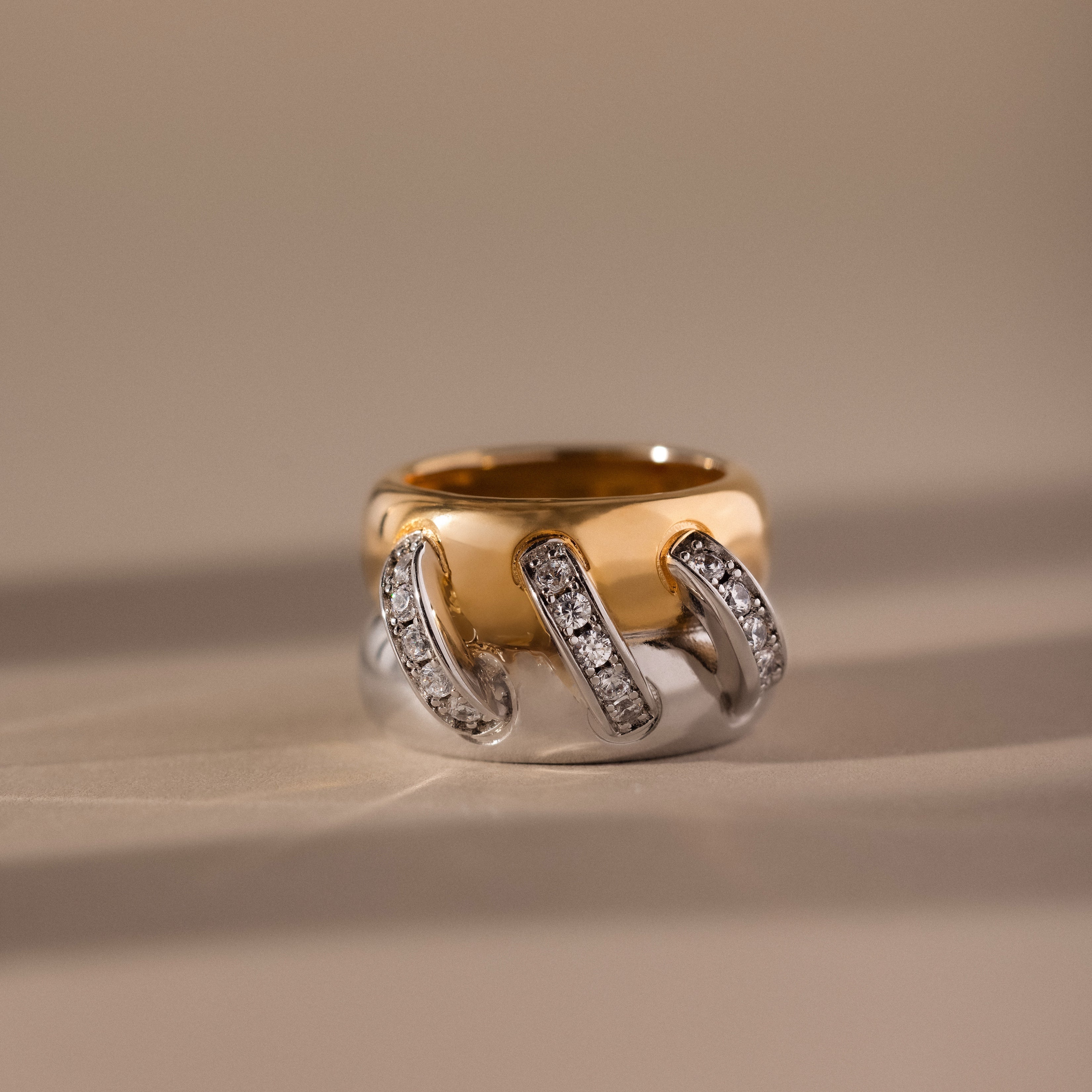 The Sculpted Mixed Metal Link Ring features gold and silver curved bands accented with pavé diamonds, creating a striking statement on any neutral background.