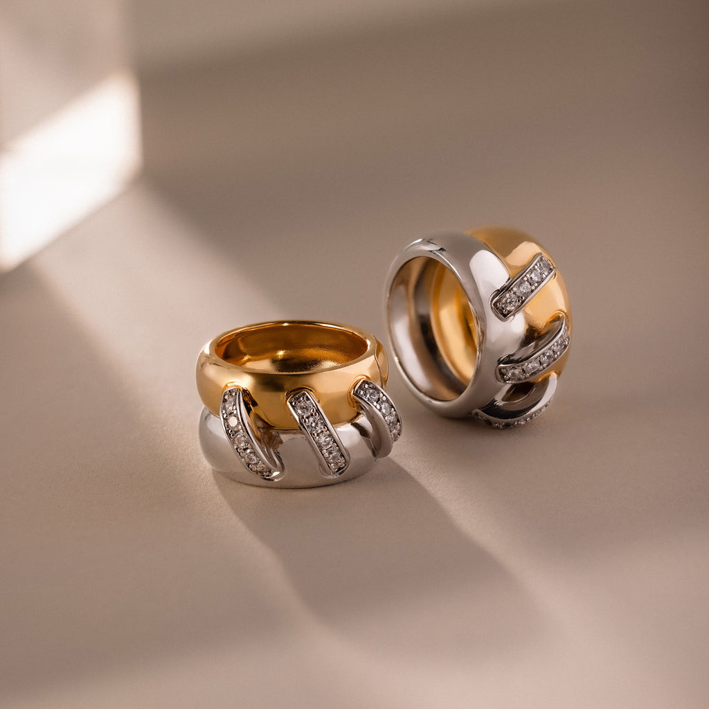 The Sculpted Mixed Metal Link Ring in gold and silver, adorned with pavé diamonds, glimmers on a neutral surface illuminated by gentle sunlight.