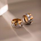 The Sculpted Mixed Metal Link Ring in gold and silver, adorned with pavé diamonds, glimmers on a neutral surface illuminated by gentle sunlight.