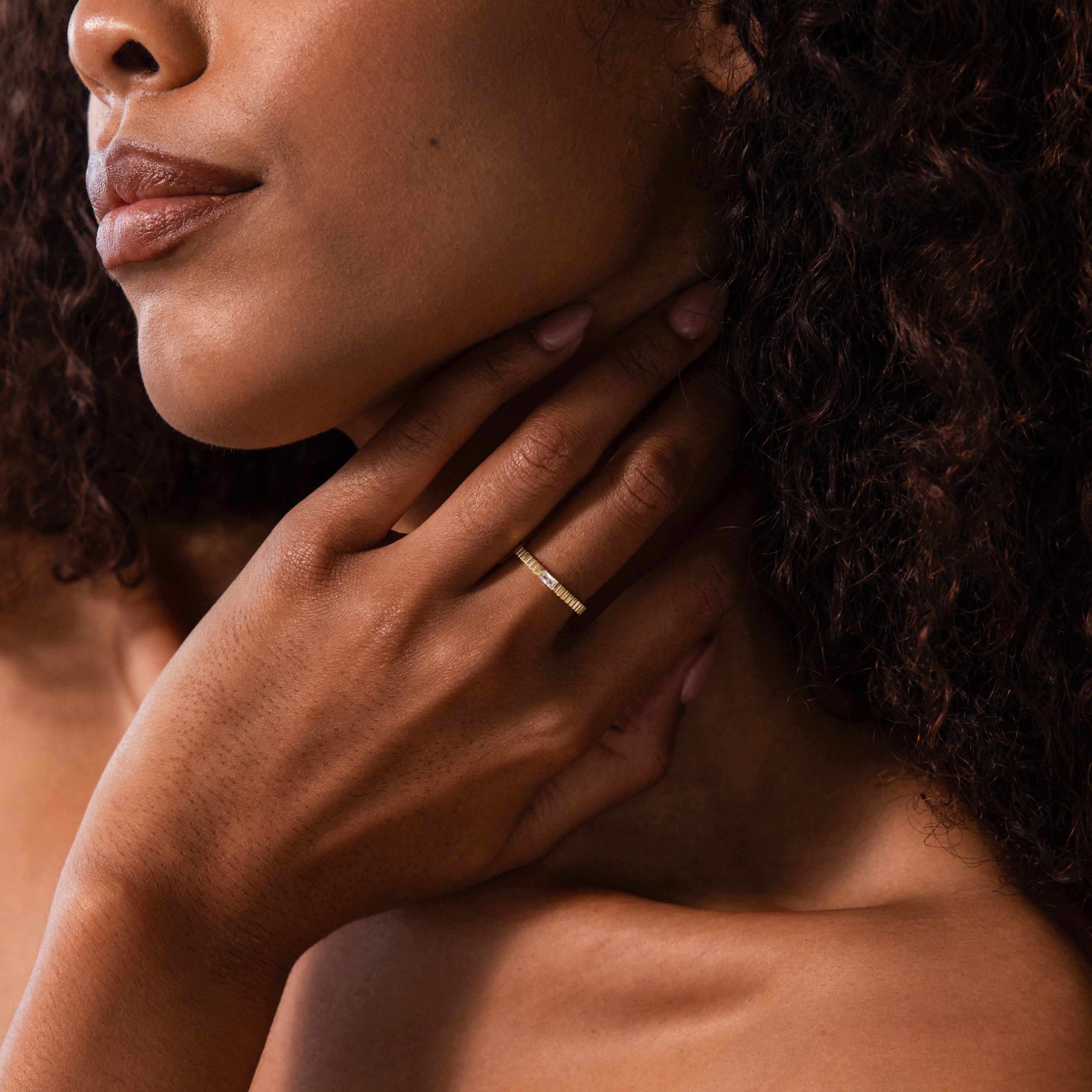 A woman with curly hair touches her neck, showcasing the Dainty Ribbed Birthstone Ring on her finger.