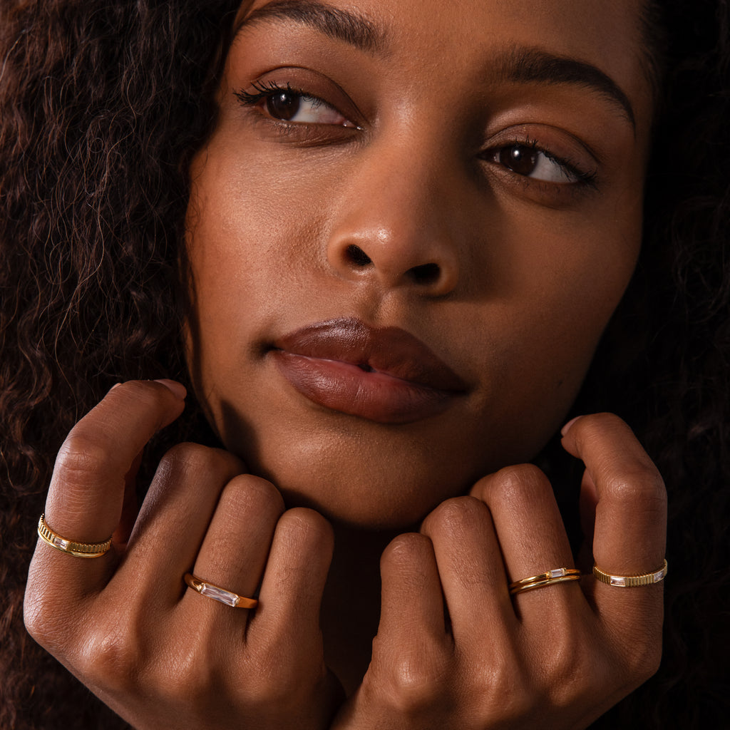 A woman with curly hair shows off a Dainty Ribbed Alexandrite Ring on her fingers, her face resting gently on her hands.