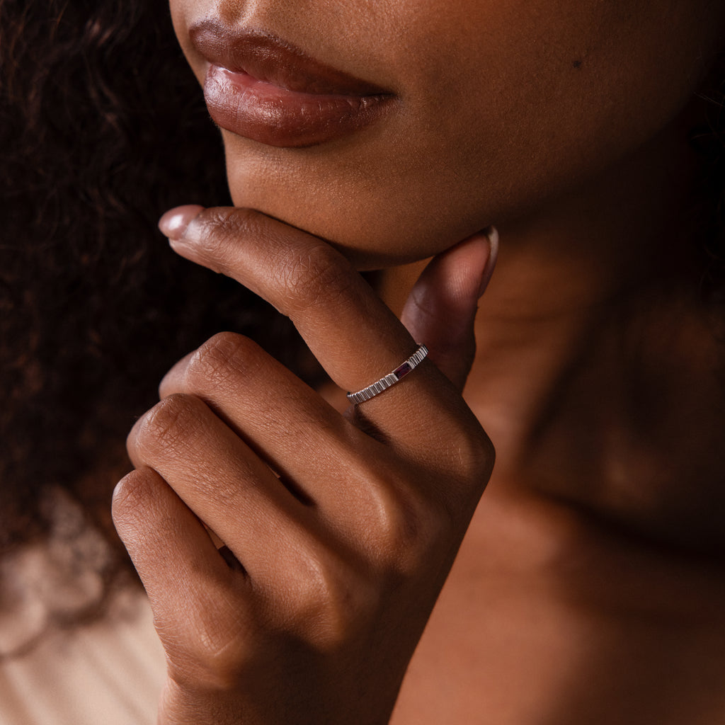 A woman with curly hair gently touches her chin, showcasing the Dainty Ribbed Ruby Ring on her finger—the delicate ruby adds a personal, vibrant touch to her look.