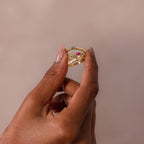 A hand holds the Dainty Ribbed Aquamarine Ring, featuring multiple gold bands and a light blue gemstone, set against a neutral background.