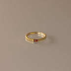 The Dainty Ribbed Garnet Ring features a ridged gold band with a small rectangular red gemstone, ideal as a delicate ring or personalized birthstone accessory, and is displayed on a neutral background.
