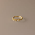 The Dainty Ribbed Diamond Ring features a slim gold ridged band and a petite rectangular diamond, perfect as a birthstone ring and shown on a neutral background.