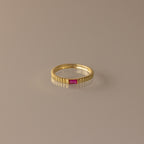 The Dainty Ribbed Ruby Ring features a gold ribbed band with a small rectangular pink gemstone at the center, ideal as a birthstone ring or for stacking.