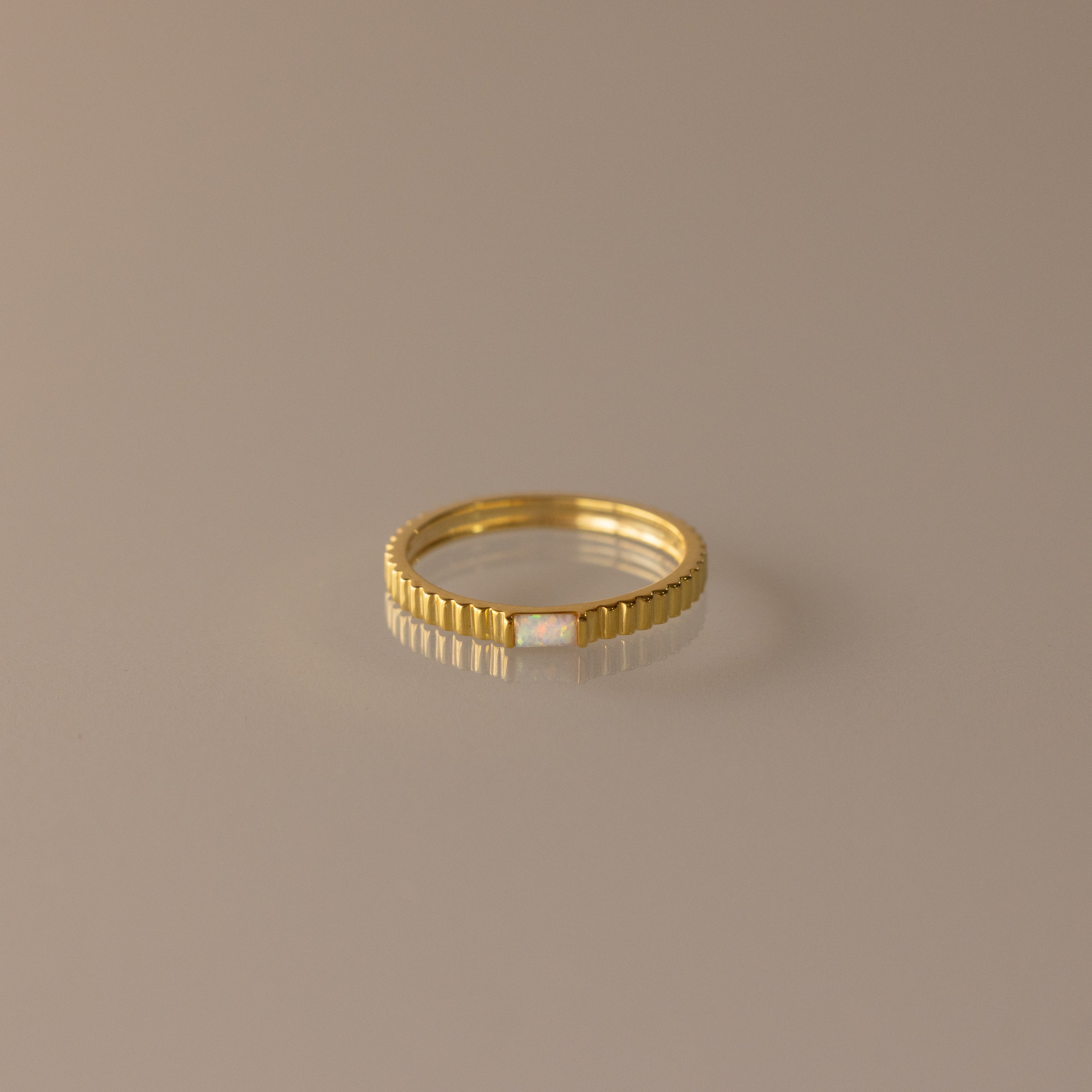 The Dainty Ribbed Opal Ring features a slim gold ribbed band with a small central opal, ideal as a delicate birthstone ring or for stacking, shown on a neutral background.