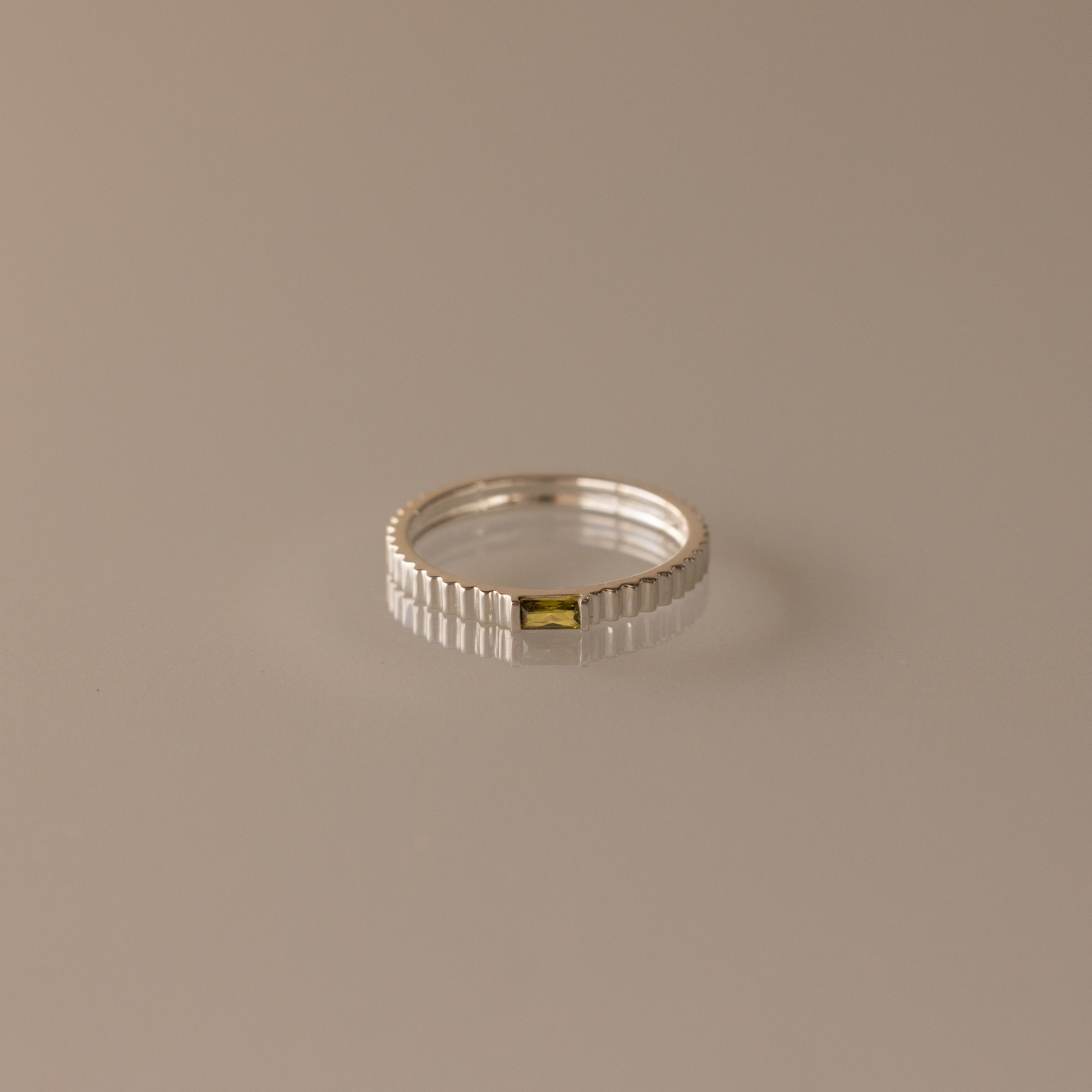 The Dainty Ribbed Peridot Ring showcases a slim silver ribbed band with a small rectangular yellow-green peridot center stone—ideal for stacking or wearing alone.