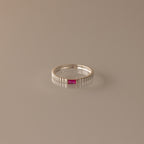 The Dainty Ribbed Ruby Ring is a delicate silver band with ribbed details, featuring a small red ruby at its center, shown against a neutral background.