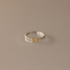 The Dainty Ribbed Topaz Ring is a delicate silver stacking piece with a ridged texture and a small rectangular yellow topaz stone set at the center.