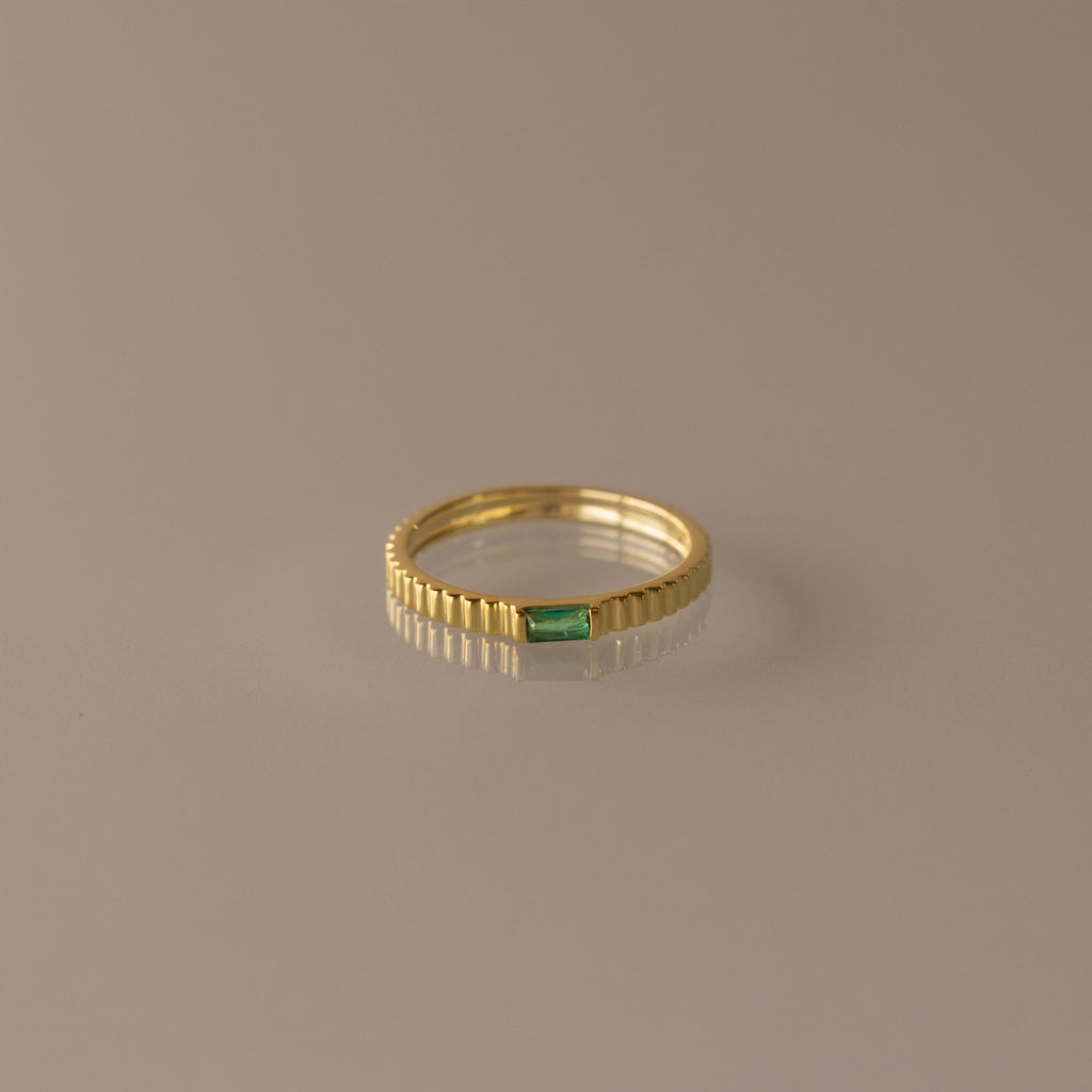 The Dainty Ribbed Emerald Ring features a small green rectangular emerald at its center, perfect for stacking and adding a touch of elegance to any look.
