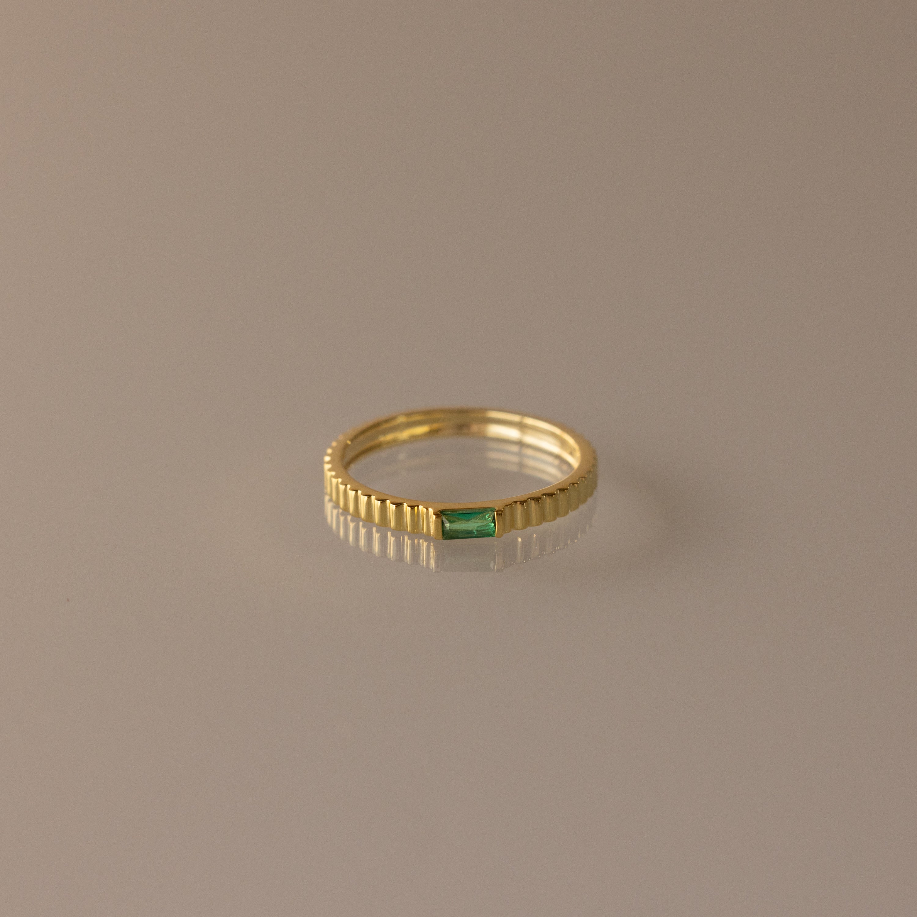 The Dainty Ribbed Emerald Ring features a small green rectangular emerald at its center, perfect for stacking and adding a touch of elegance to any look.