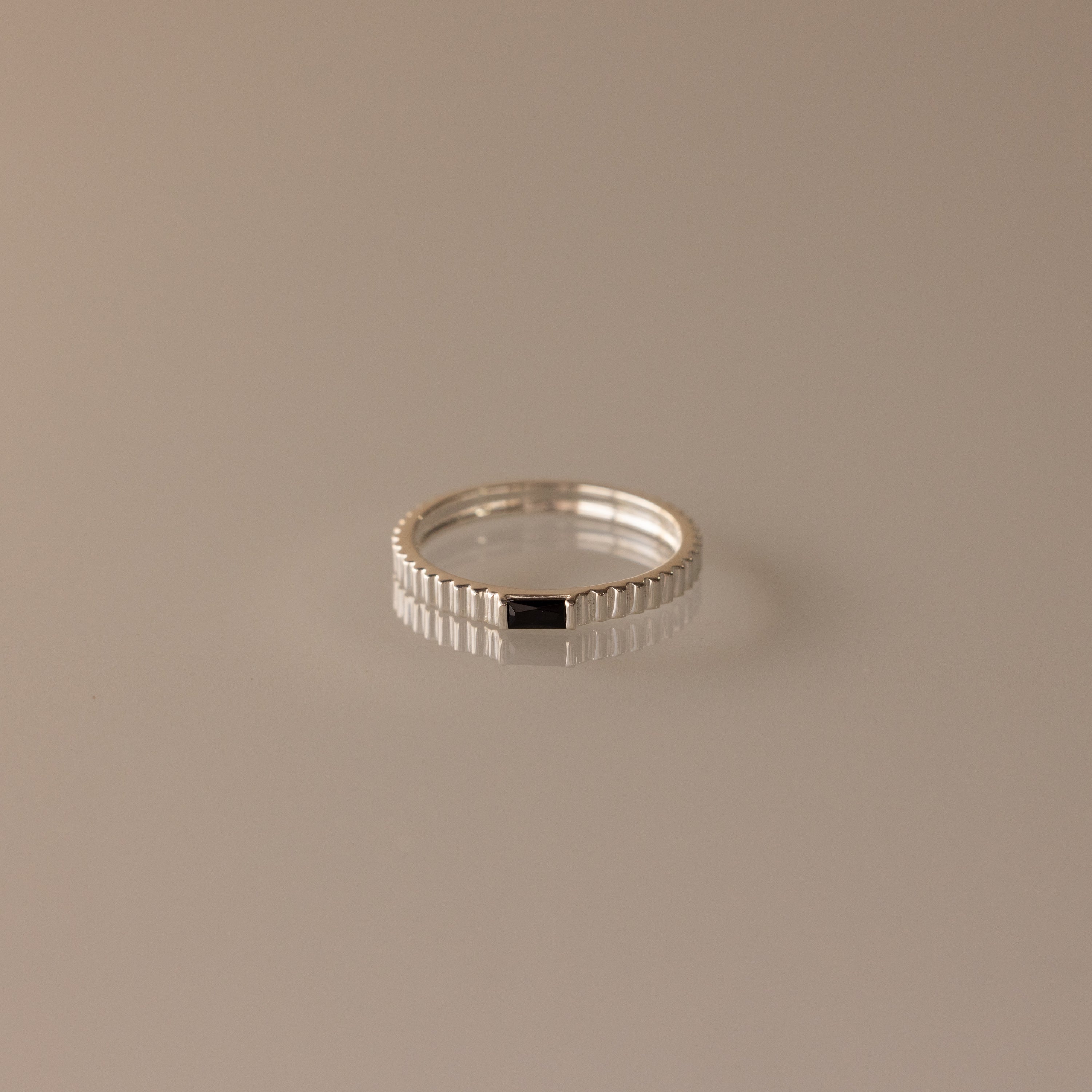 The Dainty Ribbed Onyx Ring features a textured silver band and a small rectangular black onyx stone, perfect for stacking or wearing solo. Displayed against a neutral background.