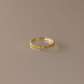 The Dainty Ribbed Alexandrite Ring features a gold ridged band and a small rectangular pale pink gemstone, ideal as a delicate ring or unique birthstone piece. Displayed on a plain surface.