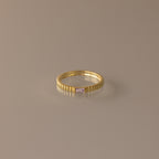 The Dainty Ribbed Alexandrite Ring features a gold ridged band and a small rectangular pale pink gemstone, ideal as a delicate ring or unique birthstone piece. Displayed on a plain surface.