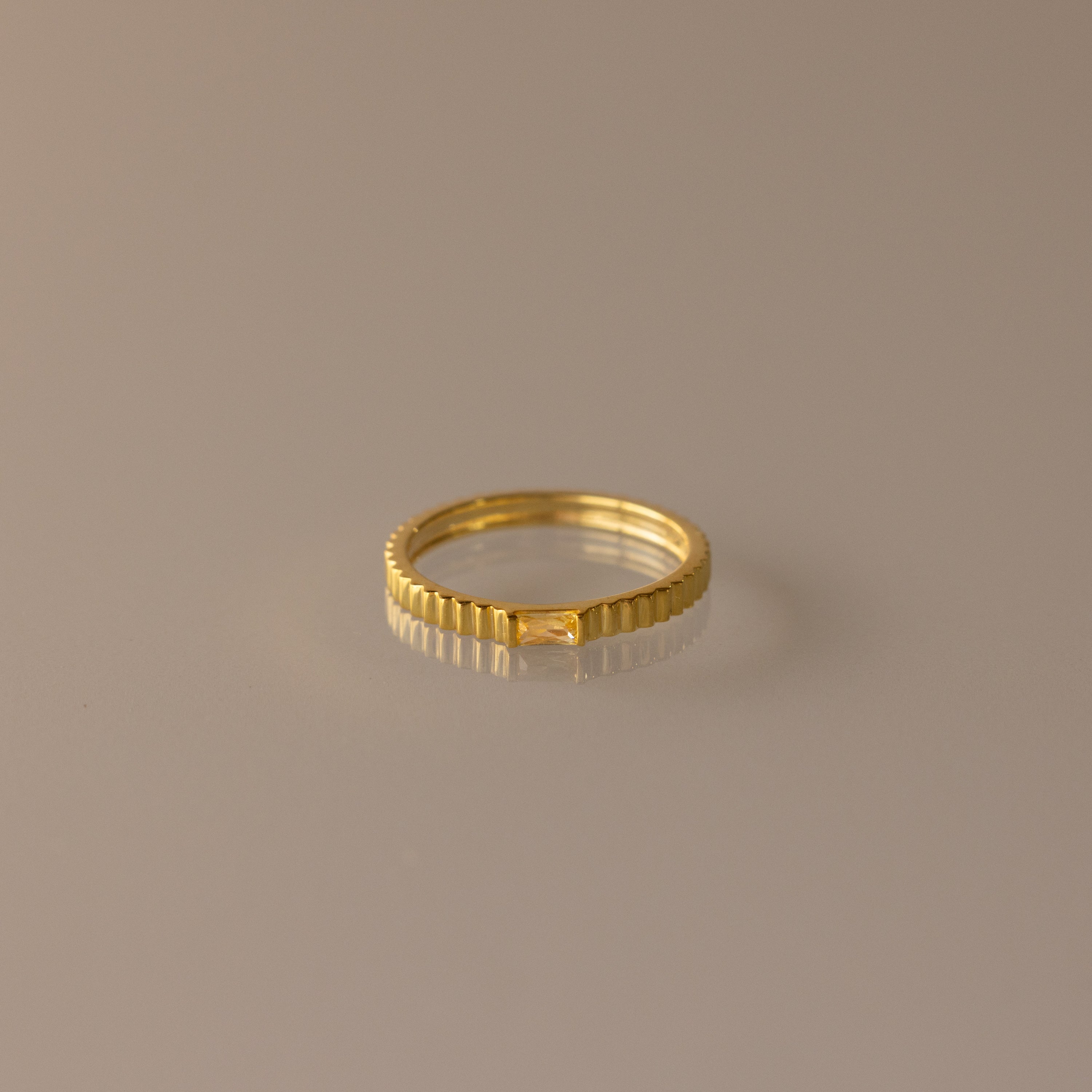 The Dainty Ribbed Topaz Ring, featuring a delicate ridged design in gold, is elegantly showcased on a neutral beige background.