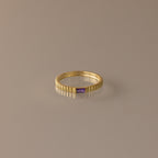The Dainty Ribbed Amethyst Ring features a gold ribbed band and a small rectangular purple amethyst, perfect for stacking or as a delicate birthstone ring. Shown on a neutral background.