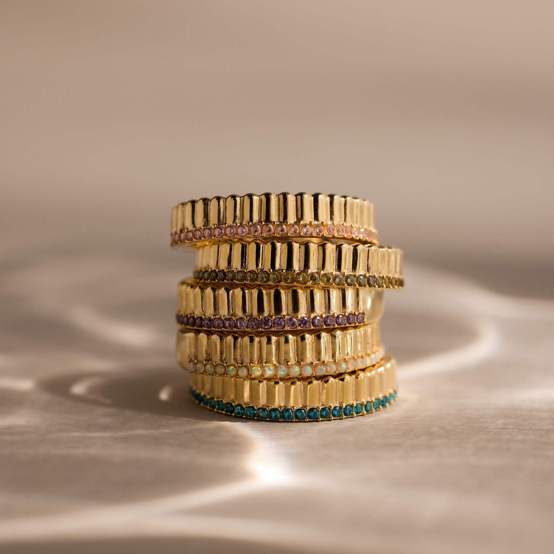 The Ribbed Alexandrite Stack Ring features a vibrant alexandrite gemstone set in a gold band, shimmering beautifully on a softly lit neutral background—perfect for stacking and adding elegance to any occasion.