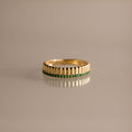The Ribbed Emerald Stack Ring is a gold band with a sculpted ribbed texture and a row of small green emeralds at the center, perfect for everyday ring stacks and shown against a plain background.