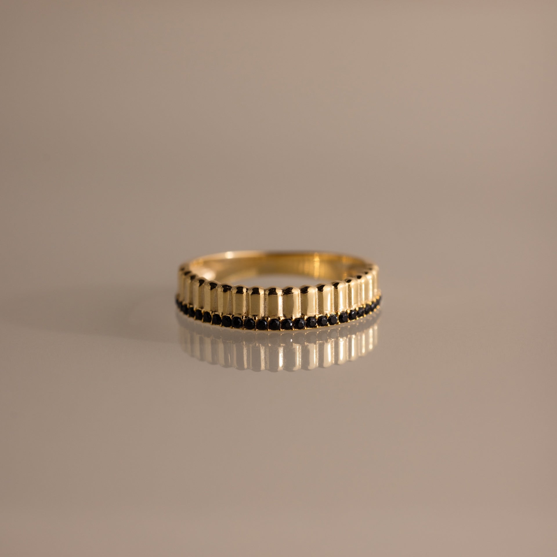 The Ribbed Onyx Stack Ring is a modern stackable ring with a gold ribbed band and a row of small black onyx stones set around the center.