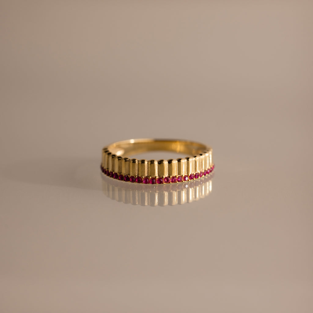 The Ribbed Ruby Stack Ring features vertical ridges and a row of small red rubies near the base, making it a unique addition to your ring stack. Shown on a neutral background.