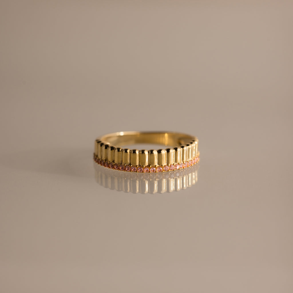 The Ribbed Pink Tourmaline Stack Ring showcases vertical grooves and a row of pink tourmalines encircling the band, its sculpted ribbed texture elegantly highlighted on a neutral surface.