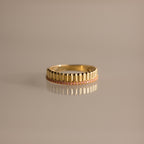 The Ribbed Pink Tourmaline Stack Ring showcases vertical grooves and a row of pink tourmalines encircling the band, its sculpted ribbed texture elegantly highlighted on a neutral surface.