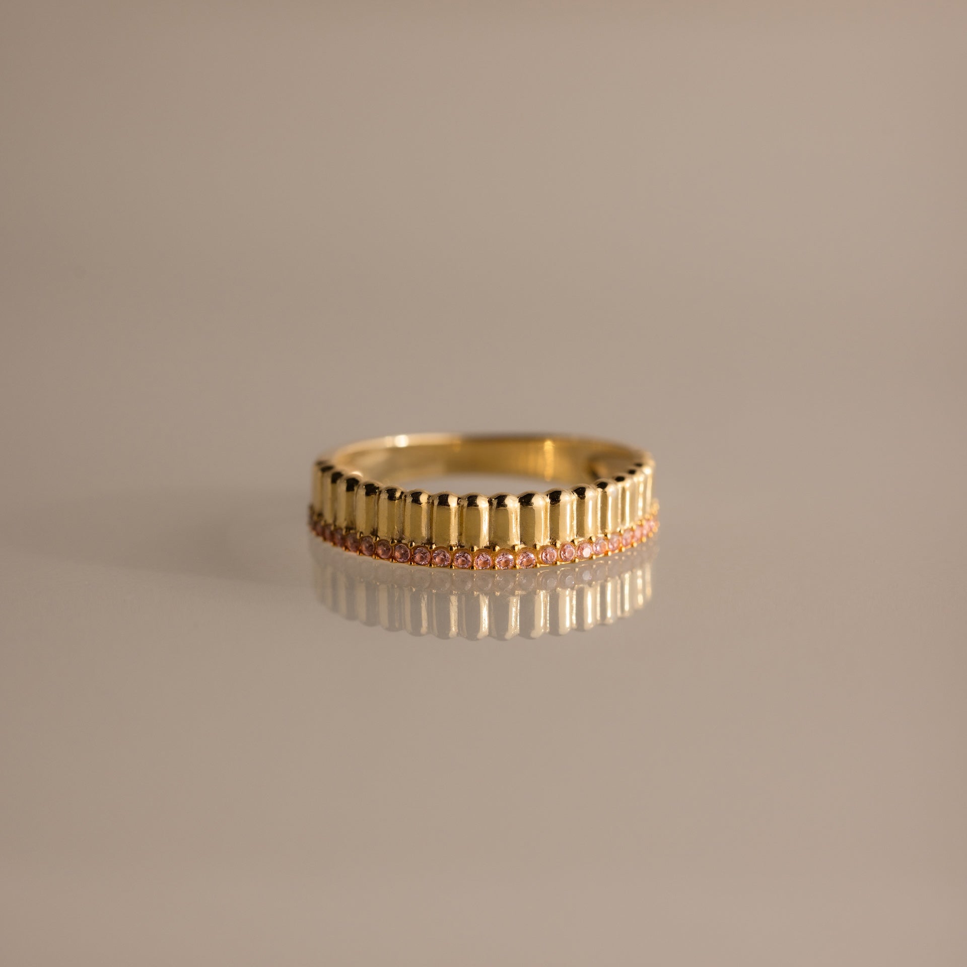 The Ribbed Pink Tourmaline Stack Ring showcases vertical grooves and a row of pink tourmalines encircling the band, its sculpted ribbed texture elegantly highlighted on a neutral surface.