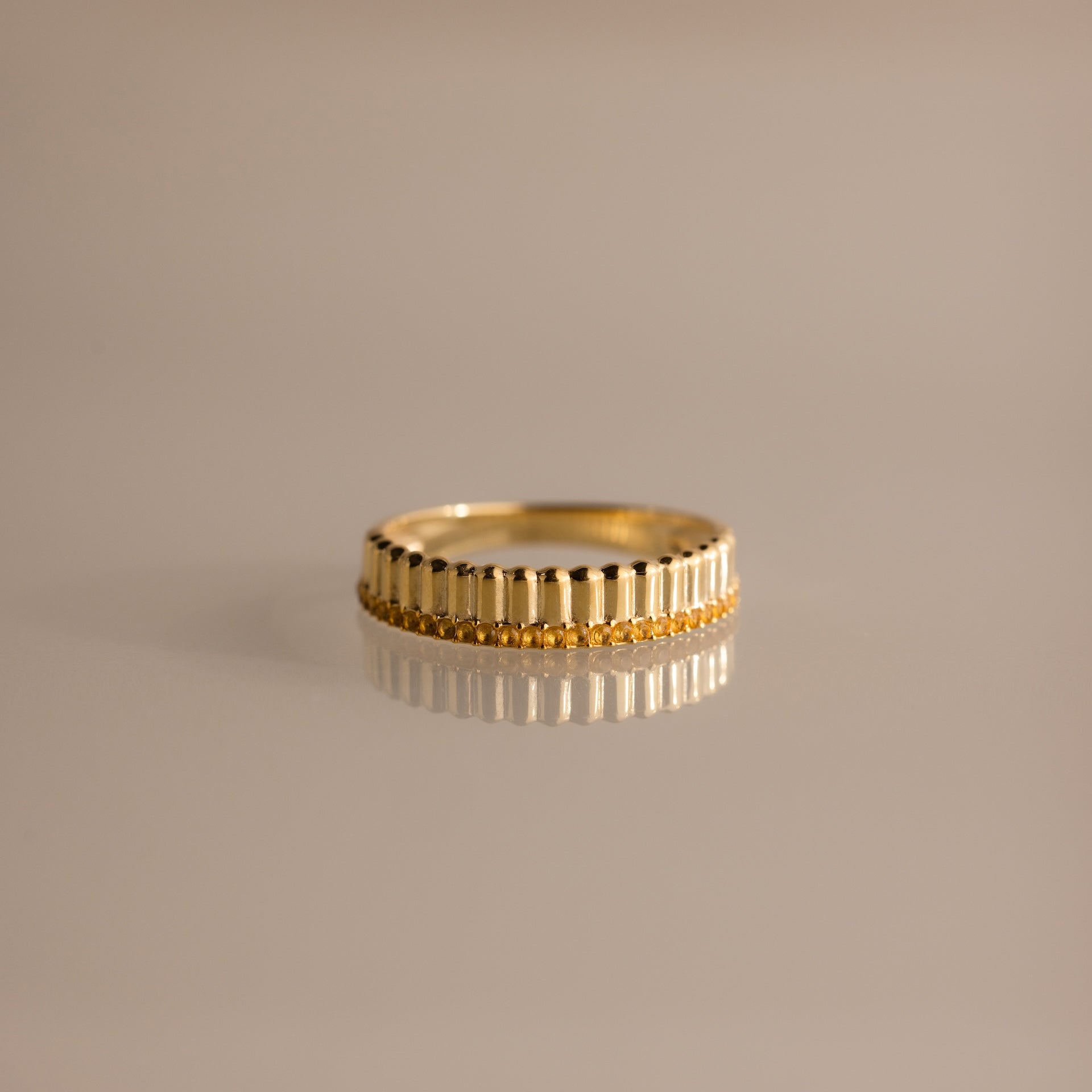 The Ribbed Topaz Stack Ring features a sculpted ribbed texture with small beads, ideal for a chic ring stack. Shown on a reflective, neutral surface.