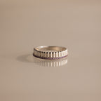 The Ribbed Alexandrite Stack Ring showcases a row of small purple stones set around the middle, elegantly displayed on a beige surface.