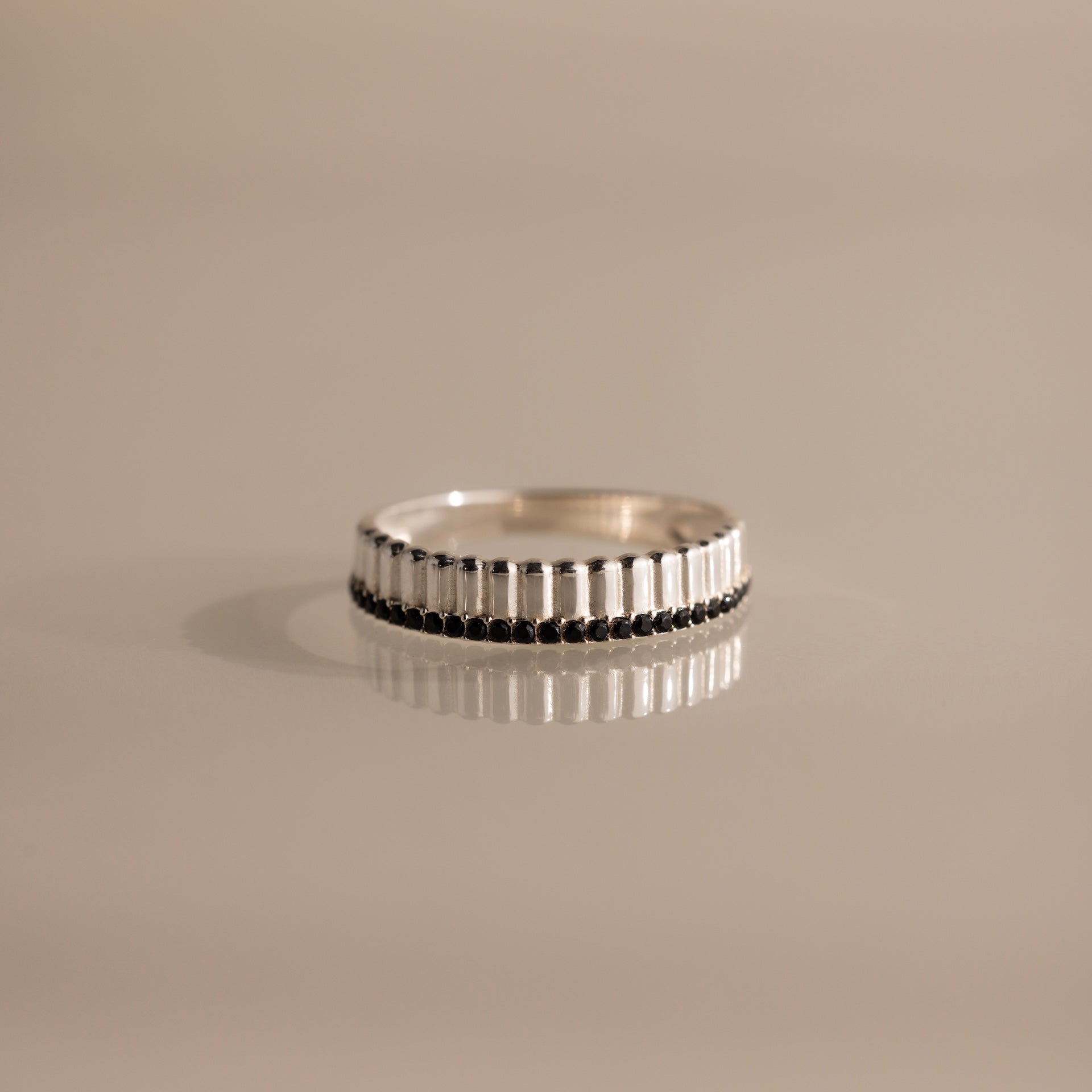 The Ribbed Onyx Stack Ring features a silver ribbed band with a row of small dark onyx stones, displayed on a neutral background.