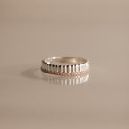 The Ribbed Pink Tourmaline Stack Ring features a sculpted ribbed texture and a row of small pink tourmaline gemstones, shown on a reflective surface. Ideal for creating your own unique ring stack style.