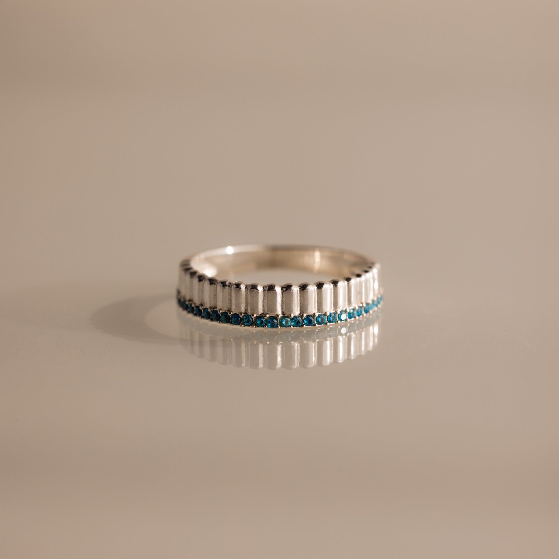 A Ribbed Blue Zircon Stack Ring, featuring a row of small blue zircon gemstones, is displayed on a neutral background.