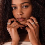A woman with curly hair poses with her hands near her face, showcasing a striking ring stack of gold and silver bands, highlighted by the Ribbed Opal Stack Ring that adds subtle ribbed texture to her elegant look.