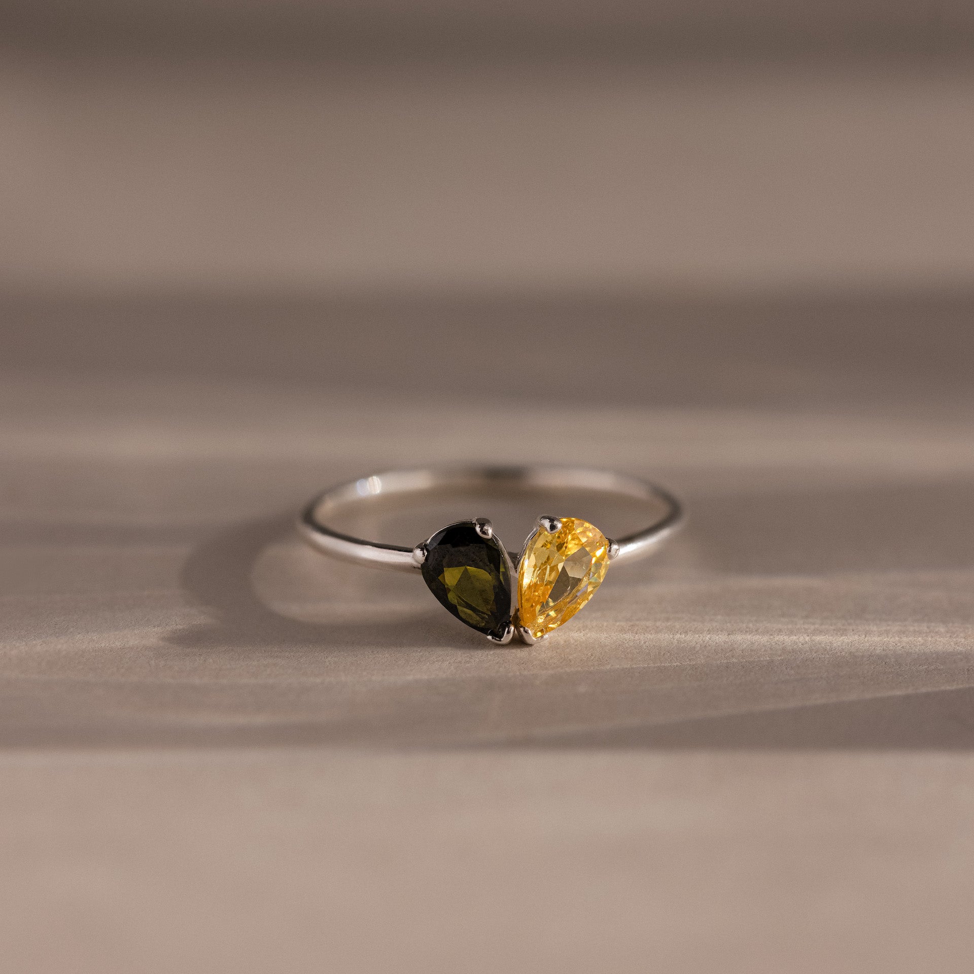 The Toi et Moi Teardrop Heart Ring showcases black and yellow pear-cut stones set side by side on a neutral surface.