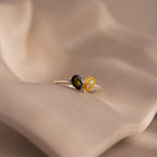 The Toi et Moi Teardrop Heart Ring in Sterling Silver, featuring black and yellow pear-cut stones, rests on a soft, beige wavy surface.