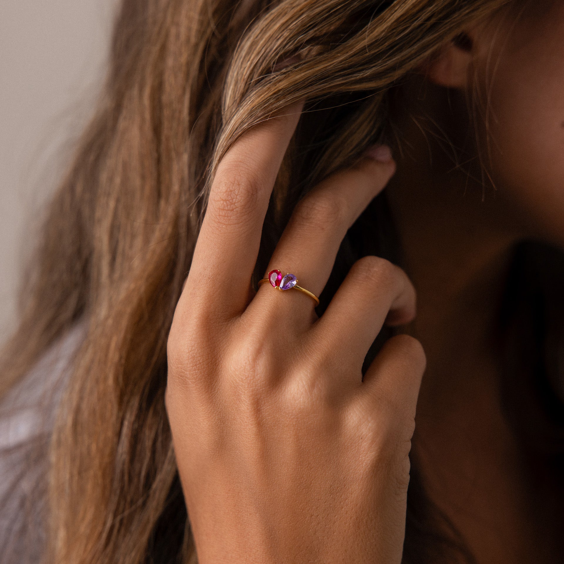 A hand with wavy brown hair wears the Toi et Moi Teardrop Heart Ring, a gold piece adorned with two pink gemstones.