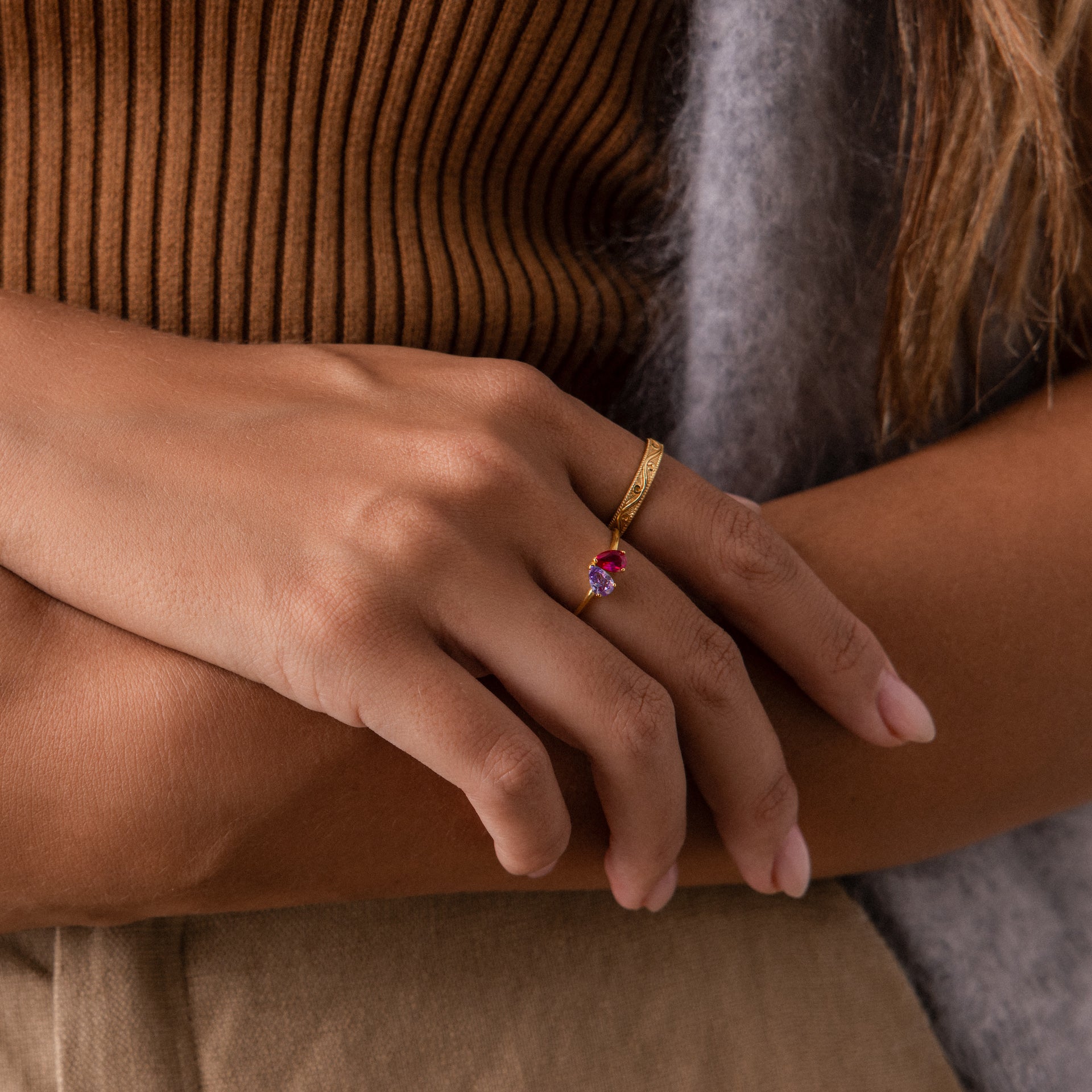 A woman's hand wearing the Toi et Moi Teardrop Heart Ring with a pink stone rests on her arm as she wears a brown top.