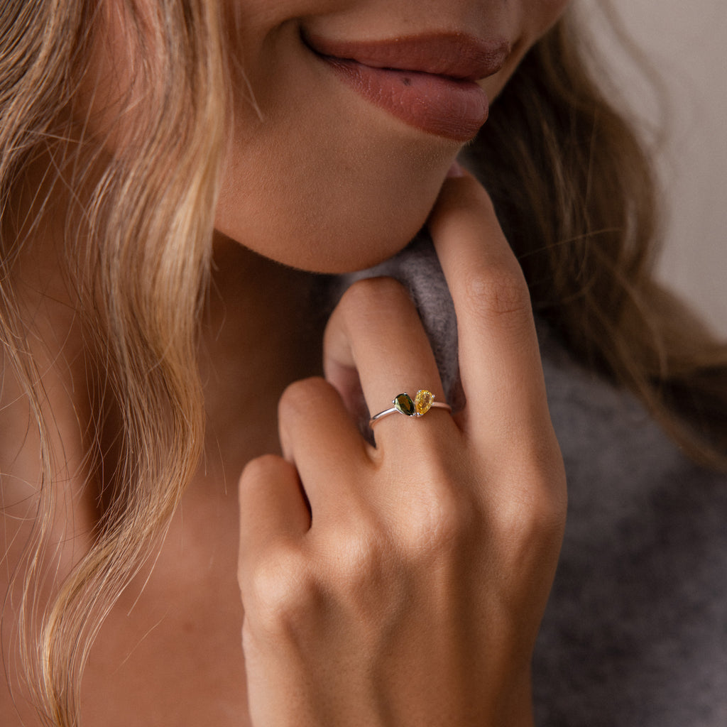 A woman smiles softly, displaying the Toi et Moi Teardrop Heart Ring in Sterling Silver with pear-cut stones on her hand near her face.