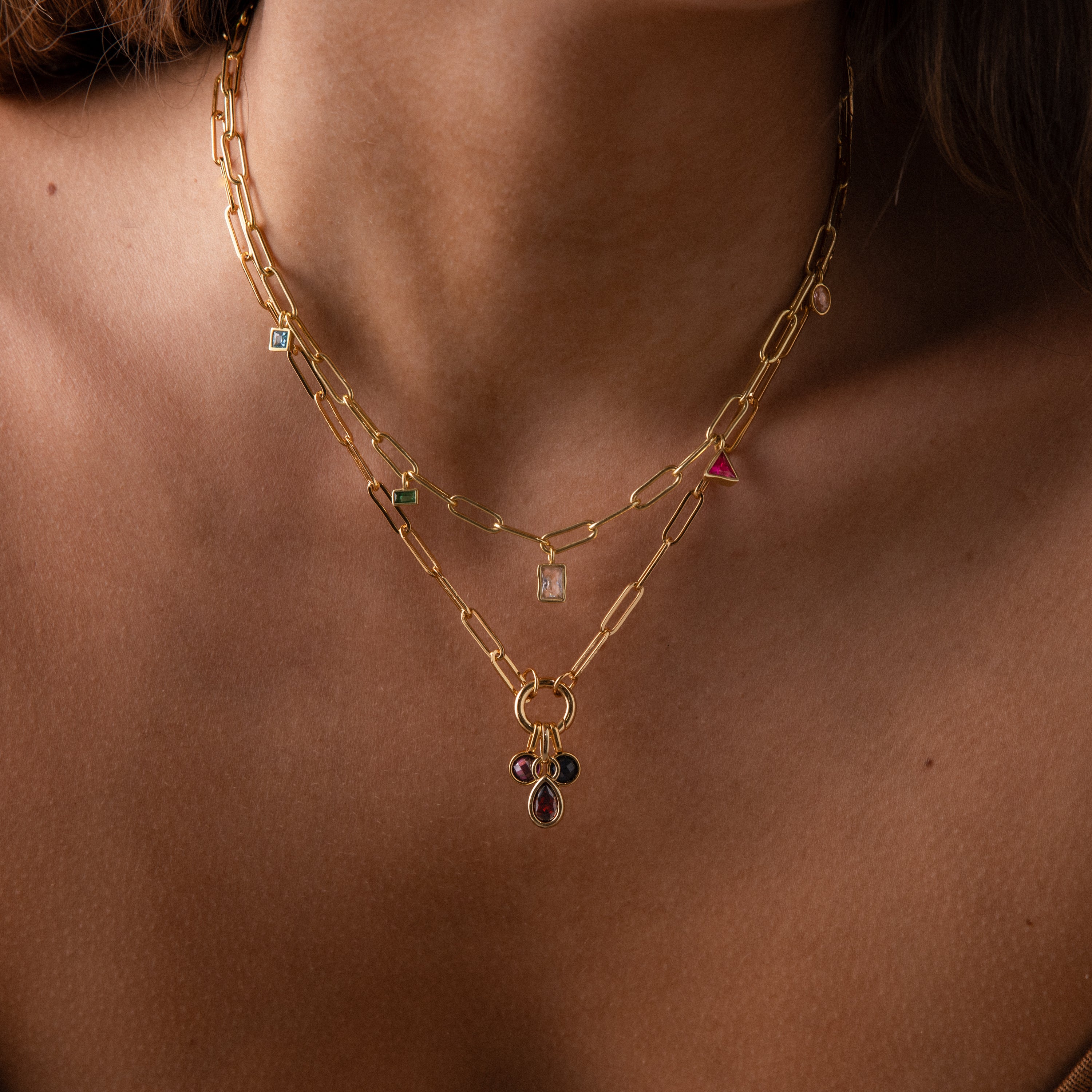 Close-up of a person wearing the Mixed Birthstone Charm Necklace, featuring layered gold chains with colorful gemstone charms and custom jewelry accents.