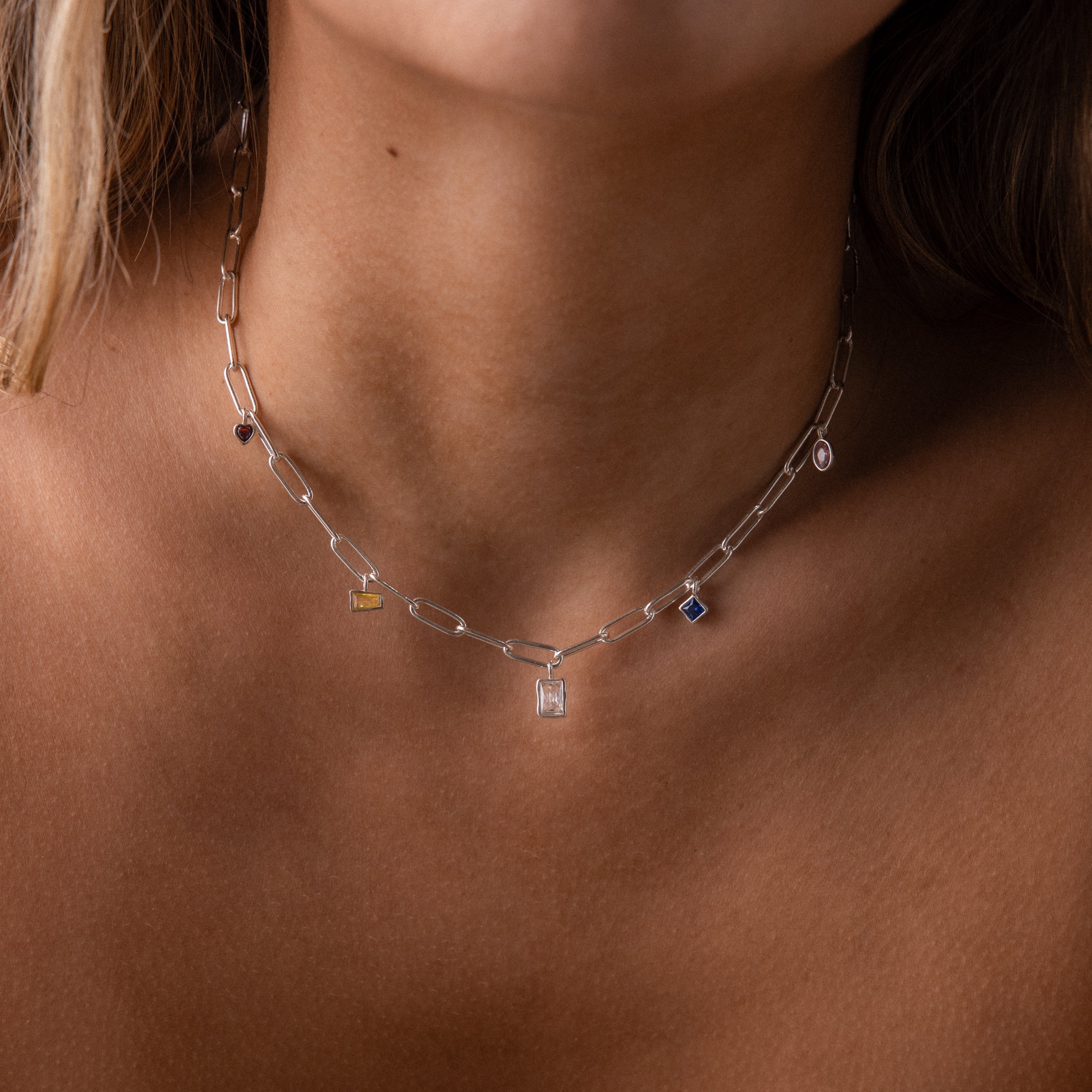 A close-up of a woman's neck wearing the Mixed Birthstone Charm Necklace in Sterling Silver, adorned with small, colorful gemstone charms.