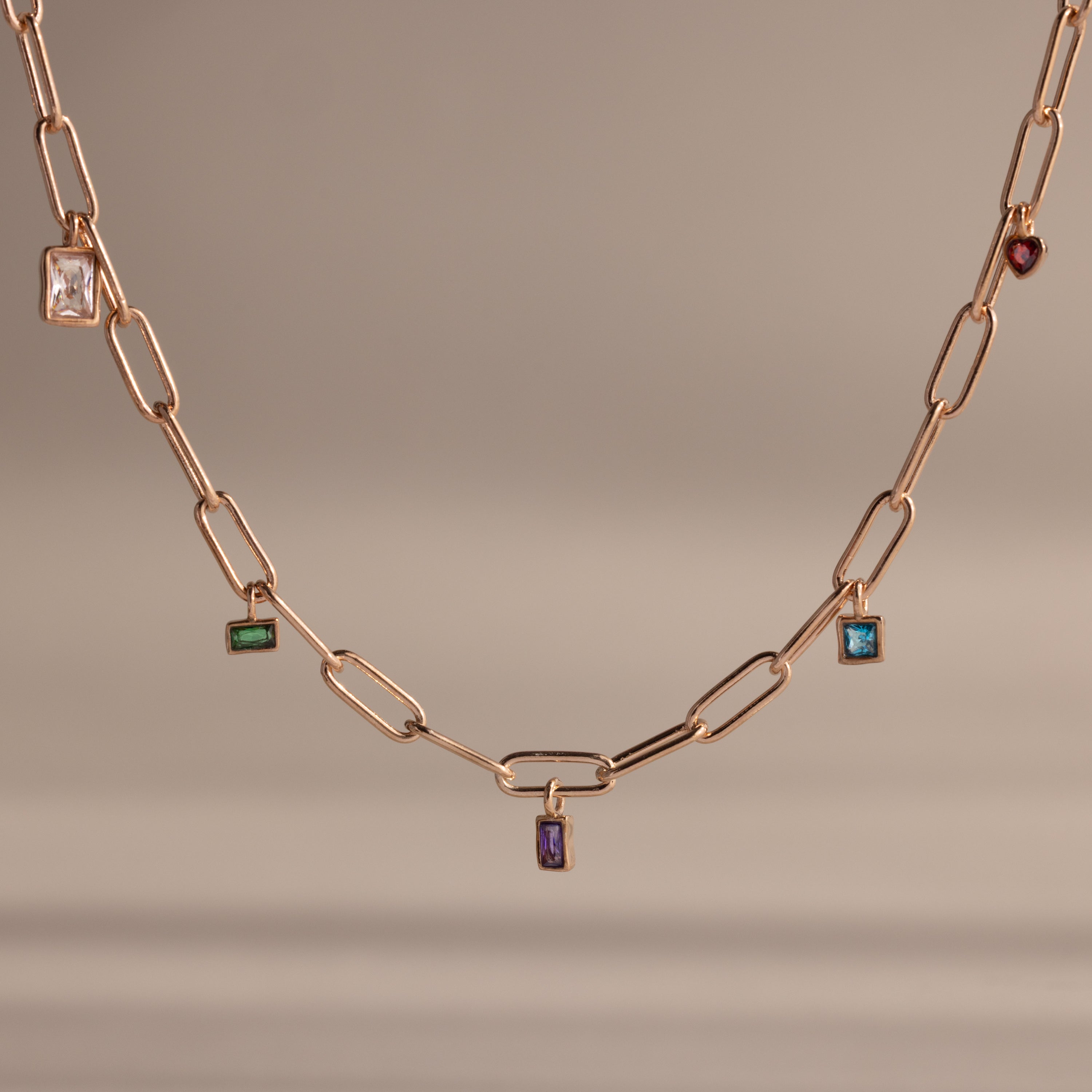The Mixed Birthstone Charm Necklace in Rose Gold showcases rectangular colored gemstones as charms on a gold chain—a stunning, personalized accessory set against a neutral background.