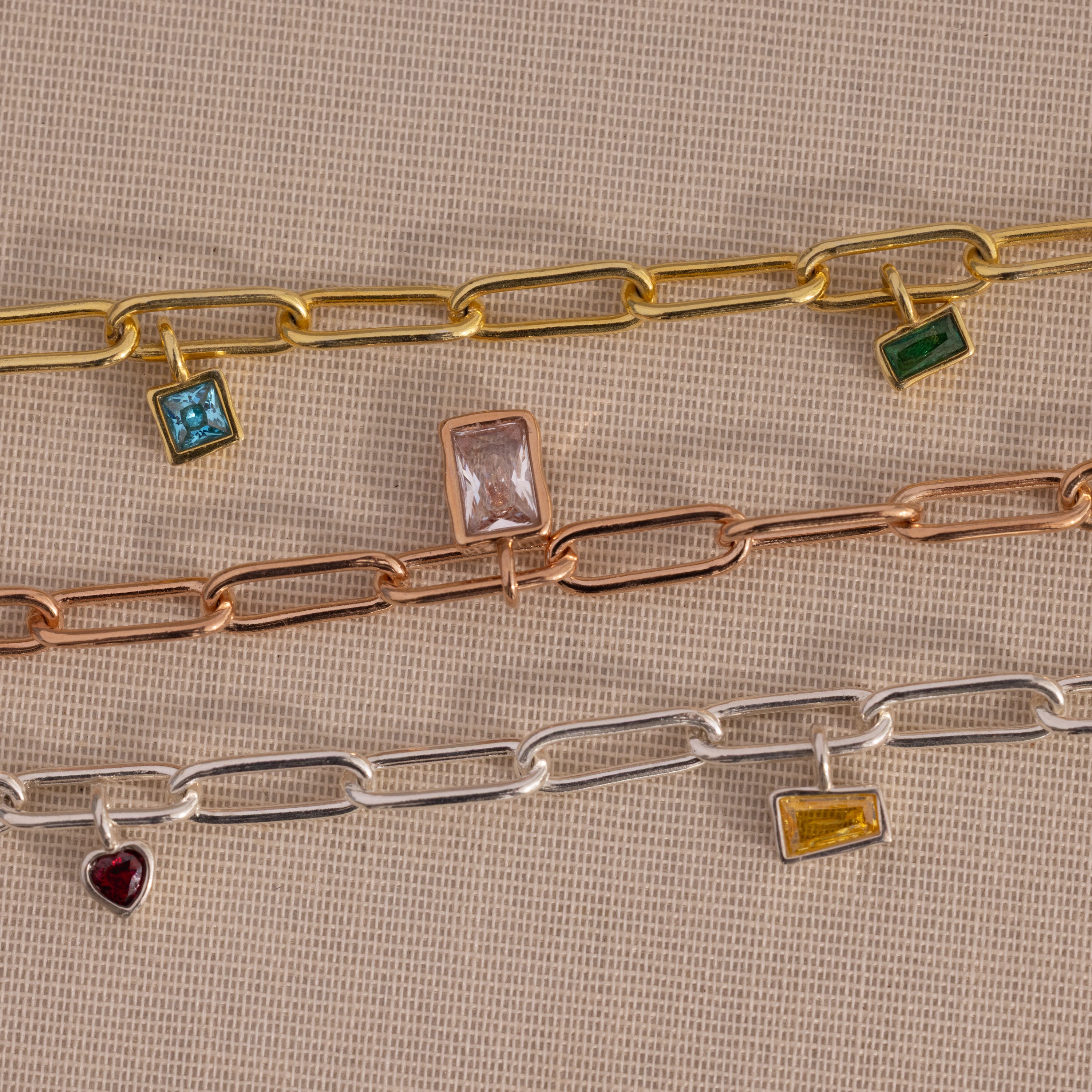 The Mixed Birthstone Charm Necklace in Rose Gold, adorned with colorful birthstone charms, captures vibrant style—displayed on a beige background.