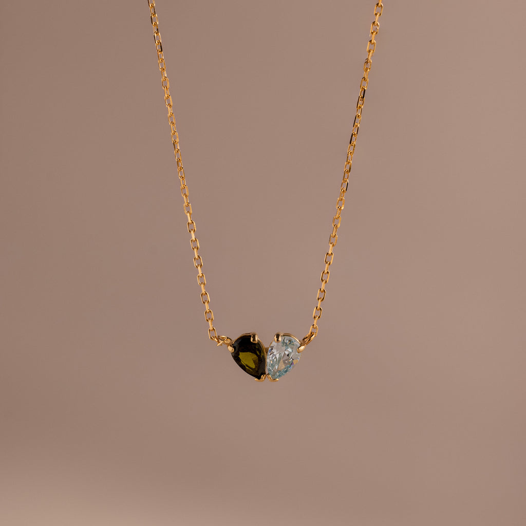 The Toi et Moi Teardrop Heart Necklace features a gold chain with a heart-shaped pendant, half black stone and half clear stone, beautifully displayed against a plain background.