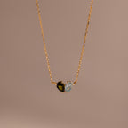 The Toi et Moi Teardrop Heart Necklace features a gold chain with a heart-shaped pendant, half black stone and half clear stone, beautifully displayed against a plain background.